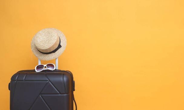 Valise noire avec lunettes de soleil, chapeau sur fond jaune pastel. concept de voyage. style minimal - Photo, image