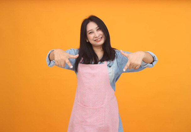 幸せなアジアの女性は黄色の背景に料理の広告のテーマのためのエプロンで料理をしています. - 写真・画像