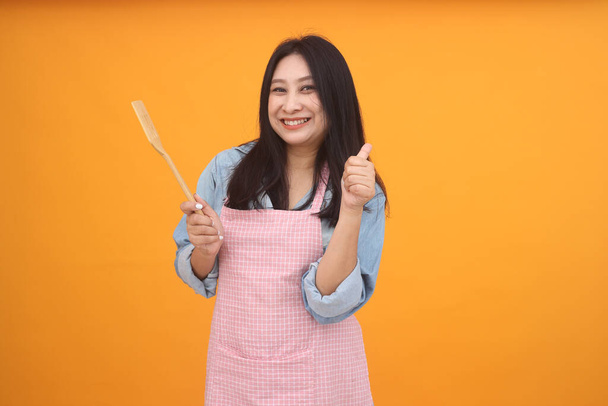 Happy Asian woman is cooking with apron for cooking advertise theme on on yellow background. - Photo, image