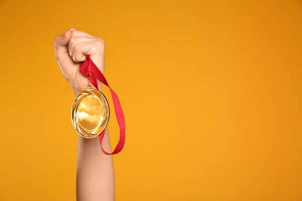 Woman holding gold medal on yellow background, closeup. Space for text - Foto, Bild