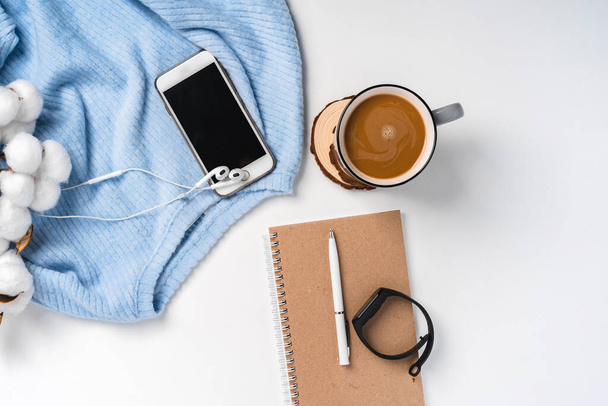  A modern creative background of a sweater, a cup of coffee, a smartphone and a branch of cotton. Cozy home working environment - Photo, Image