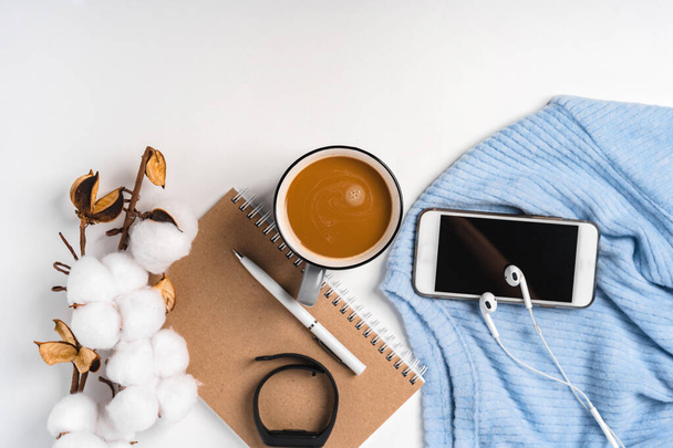  A modern creative background of a sweater, a cup of coffee, a smartphone and a branch of cotton. Cozy home working environment - Foto, imagen