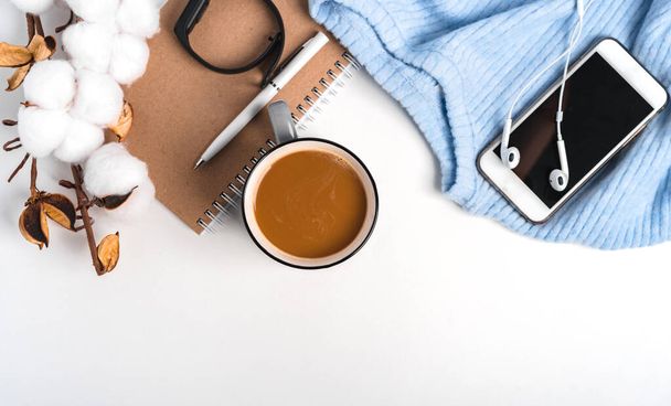  Un fondo creativo moderno de un suéter, una taza de café, un teléfono inteligente y una rama de algodón. Acogedor ambiente de trabajo en casa - Foto, imagen