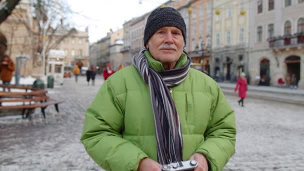 Älterer Mann fotografiert mit Fotokamera und lächelt mit Retro-Gerät in der winterlichen Innenstadt - Filmmaterial, Video