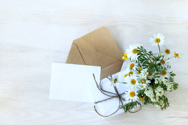 open envelope with a blank sheet next to a gift and a bouquet of wild flowers top view / festive set for congratulations - Fotoğraf, Görsel