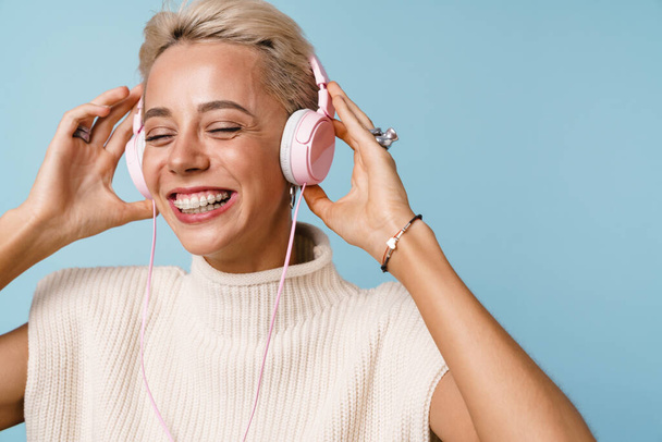 Cheerful beautiful girl listening music with headphones isolated over blue background - Fotoğraf, Görsel