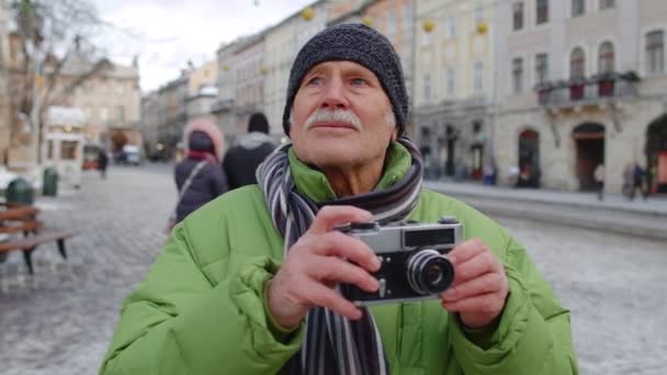 Vanhempi onnellinen mies isoisä ottaa kuvia valokuvakameralla, hymyillen retro-laitteella ulkona - Materiaali, video