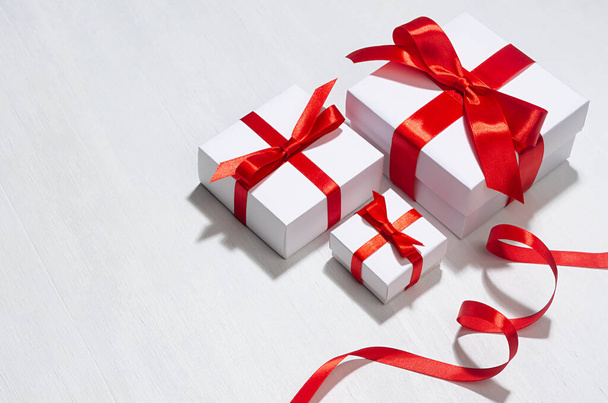 Minimalist elegant three New Year white gift boxes with red bow on white wood board as border. - Фото, зображення