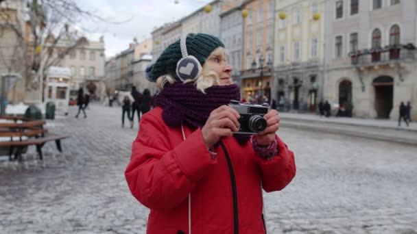Yaşlı kadın turist fotoğraf makinesiyle fotoğraf çekiyor, retro cihazla gülümsüyor. - Video, Çekim