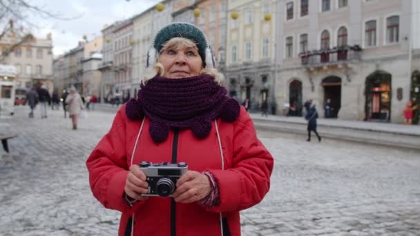 Turista senior tomando fotos con cámara fotográfica, utilizando dispositivo retro en la ciudad de invierno, bloqueo - Imágenes, Vídeo