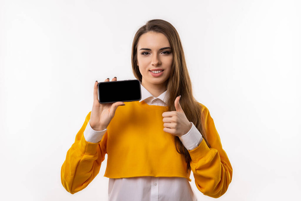 Ezt figyeld! Csinos fiatal barna nő alkalmi ruhát mutat okostelefon üres képernyő a kezében. Lány ajánlja feltölteni az új alkalmazást, online vásárlás oldalon. Készíts másolási helyet. - Fotó, kép