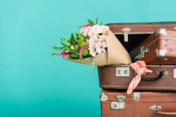 トルコ石で隔離された新鮮な花やヴィンテージのスーツケースの花束 - 写真・画像