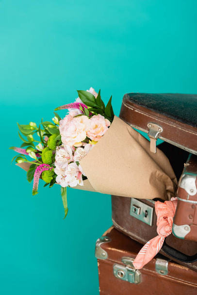 boeket van verse bloemen en vintage koffers geïsoleerd op turquoise - Foto, afbeelding