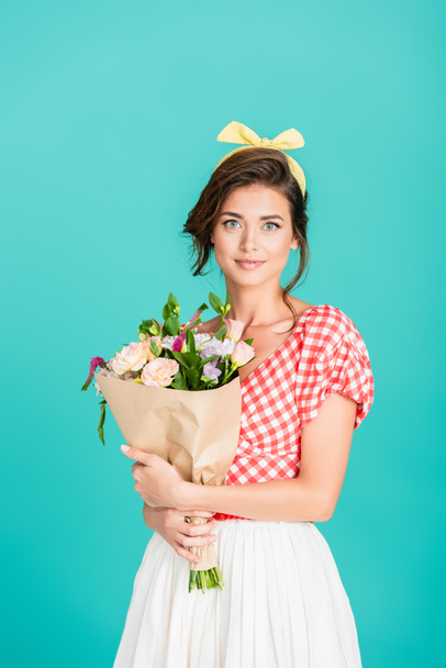 happy pin up woman smiling at camera while holding fresh bouquet isolated on turquoise - Fotografie, Obrázek