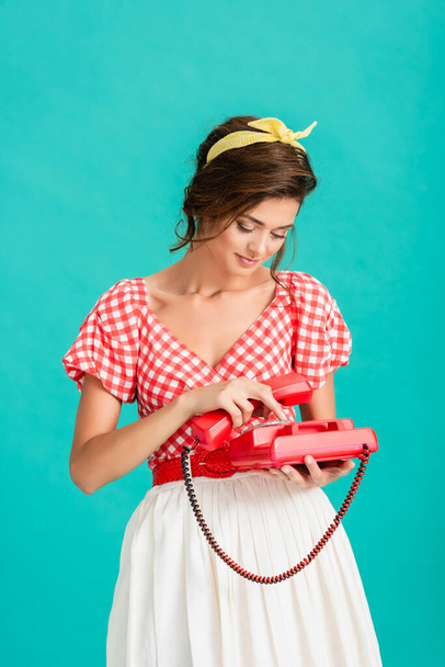 молода жінка в стильному ретро одязі закликає на старовинний телефон ізольовано на бірюзовому
 - Фото, зображення