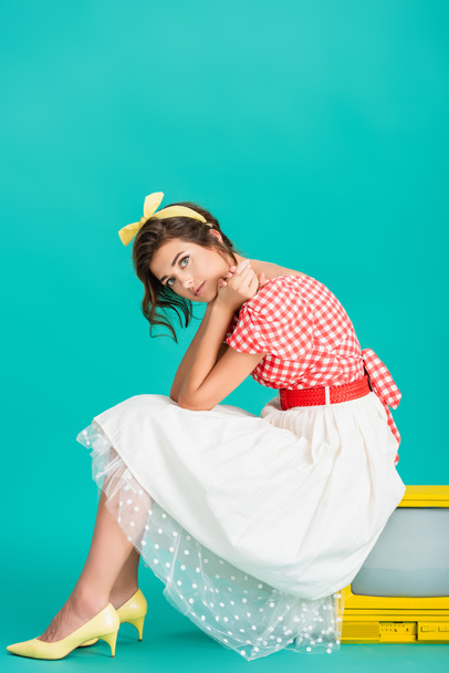 trendy pin up woman sitting on yellow retro tv and looking at camera on turquoise - Foto, Imagem