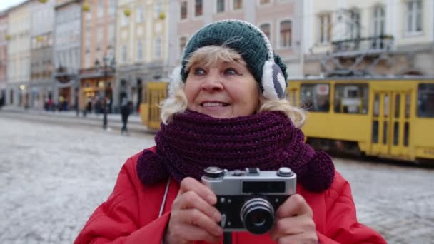 Kış şehir merkezinde retro cihaz kullanarak fotoğraf makinesiyle fotoğraf çeken yaşlı bir turist. - Video, Çekim