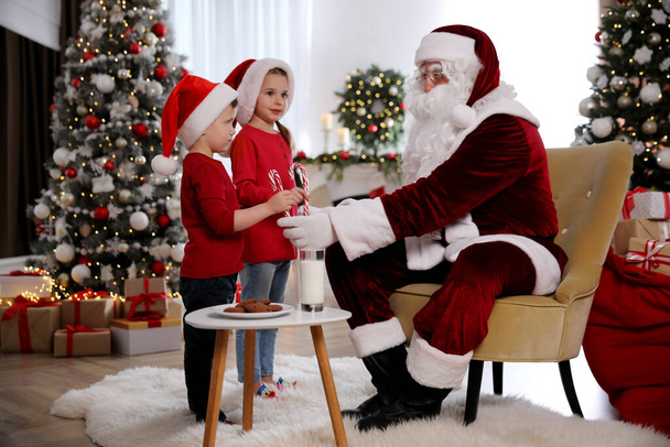 Santa Claus giving candy canes to children in room decorated for Christmas - Foto, afbeelding