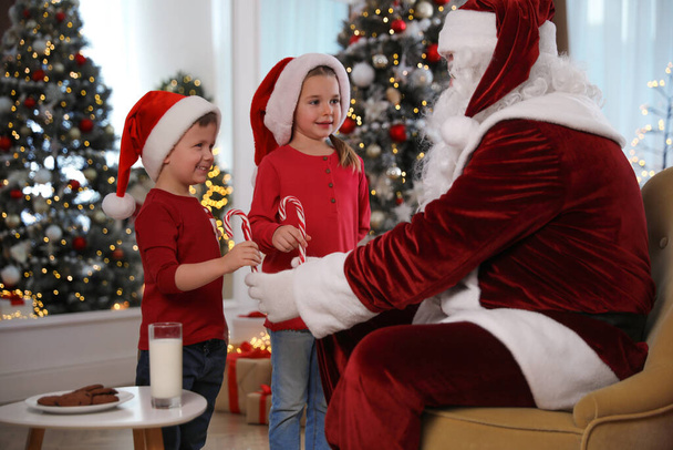 Santa Claus giving candy canes to children in room decorated for Christmas - 写真・画像