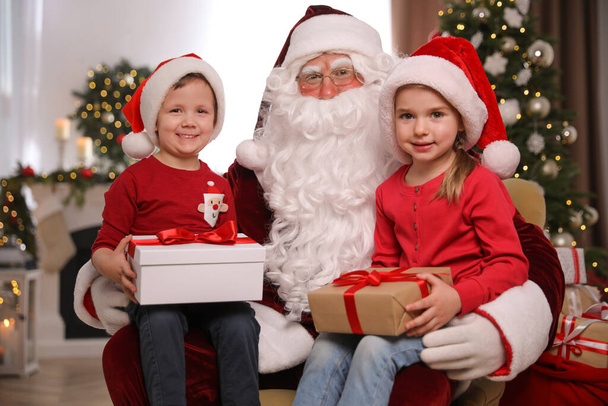 Santa Claus and little children with presents in room decorated for Christmas - Photo, image