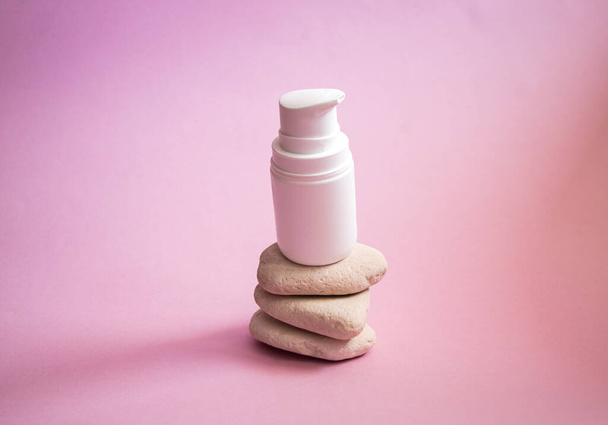 a white plastic jar with a dispenser and a gentle caring organic hand and body cream, on smooth textured rounded stones on a pink background. - 写真・画像