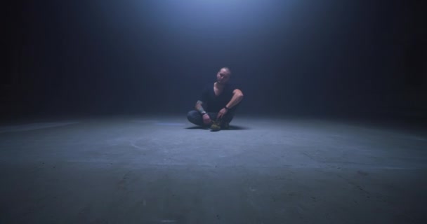 Getatoeëerde man zittend in donkere kamer - Video
