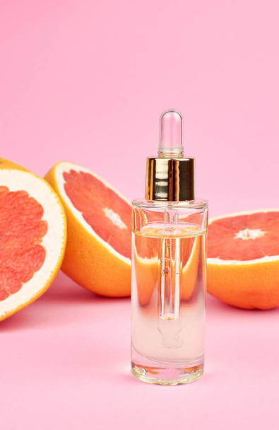 Grapefruit essential oil in glass bottle on grapefruit slices on pink background. - Foto, imagen