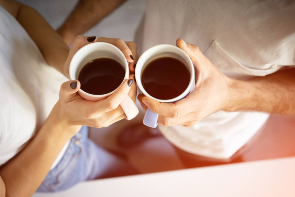 Vista superior. Duas mãos com copos de café segurando pelo jovem casal de pé na manhã na cozinha.  - Foto, Imagem