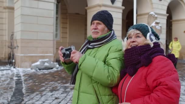 Yaşlı çift turistler, büyükanne büyükbaba. Kış şehrinde retro kamerayla fotoğraf çekiyor. - Video, Çekim