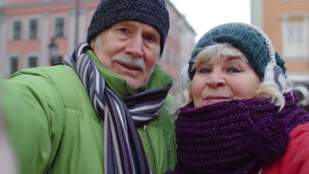 Couple de touristes âgés prenant selfie dans le centre-ville d'hiver souriant, regardant la caméra, blog, vlog - Séquence, vidéo