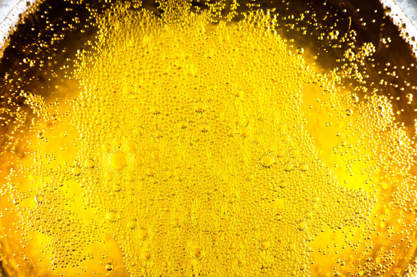 Liquid gold-yellow gasoline bubbles background on beer or champagne glass. Close up, macro shot. - Photo, Image