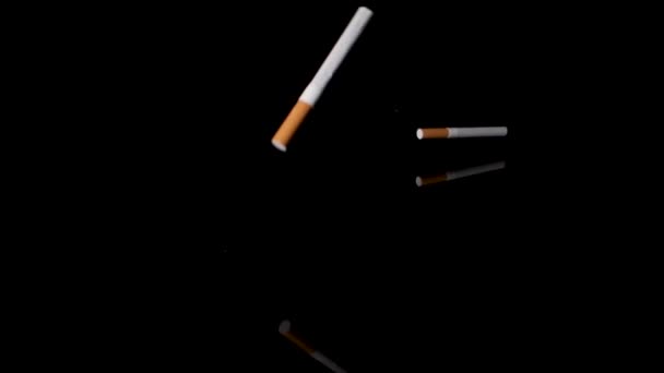 Πολλά τσιγάρα ρίχνουν κάτω στη μαύρη επιφάνεια καθρεφτισμού σε αργή κίνηση. - Πλάνα, βίντεο