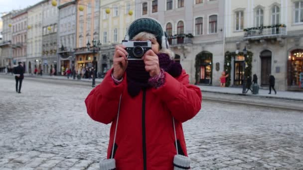 Turista senior tomando fotos con cámara fotográfica, utilizando dispositivo retro en el centro de la ciudad de invierno - Metraje, vídeo