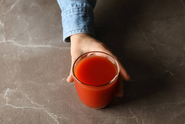 Female hand hold glass of tomato juice on gray background - Photo, Image