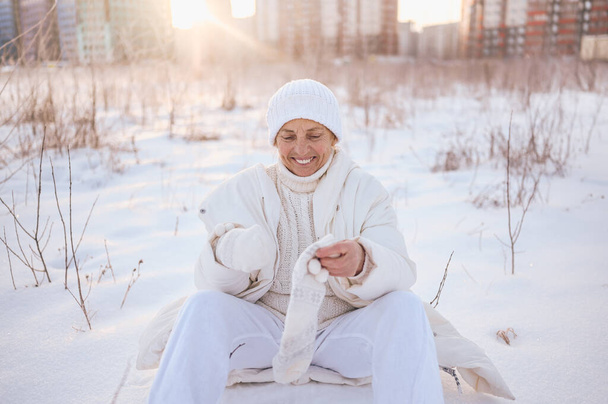 Happy elderly senior mature woman in white warm outwear playing with snow in sunny winter outdoors. Retired healthy people holiday vacation winter activities, active lifestyle concept - Photo, Image