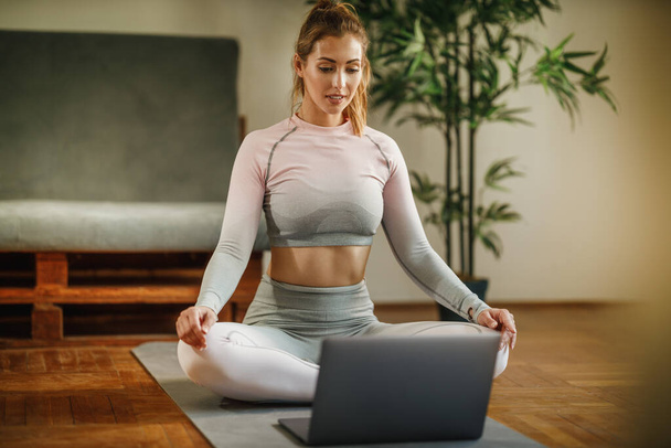 Uma jovem atraente usando laptop enquanto faz exercícios em casa durante o dia. - Foto, Imagem