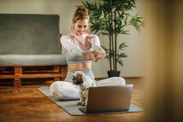 Eine attraktive junge Frau, die ihr Vlog über gesundes Leben mit dem Laptop aufzeichnet, während sie zu Hause Übungen macht. - Foto, Bild