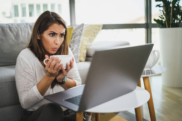 Беспокойная молодая женщина пьет послеобеденный чай и проводит онлайн-консультации с психотерапевтом у себя дома во время пандемии ковида-19. - Фото, изображение