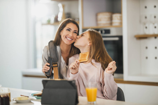 Cute teenage girl and her smiling mother is greet each other at her home while mom getting ready to go to work. - Φωτογραφία, εικόνα