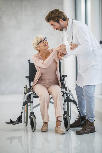 Foto di un giovane medico che aiuta una paziente anziana su una sedia a rotelle. - Foto, immagini