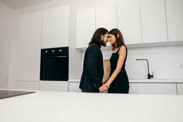 Hermosa pareja en casa en la cocina tocándose con la frente y tomándose de la mano - Foto, Imagen