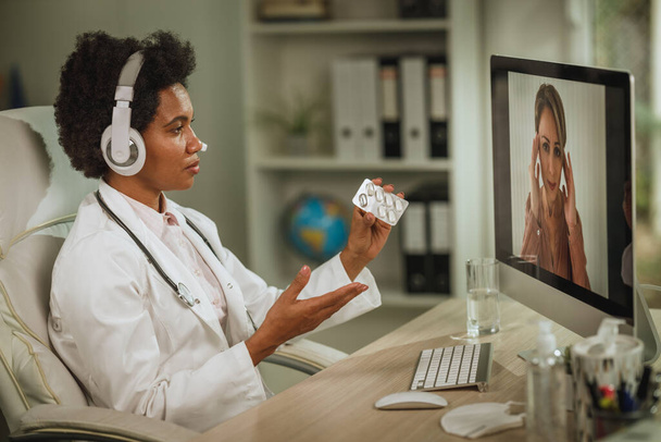Afrikkalainen naislääkäri, jolla on videopuhelu potilaan kanssa tietokoneella COVID-19-pandemian aikana. - Valokuva, kuva