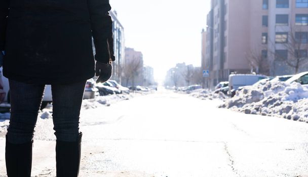 In the foreground,a woman with her back turned, dressed in dark clothing and wearing high boots.She is alone,isolated at the beginning of a street. All around her is out of focus and with a nice light - Photo, Image