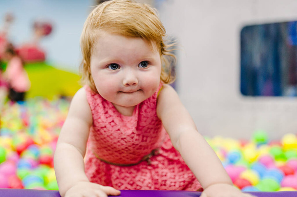 Portrait little cute baby girl princess infant 1-2 year standing and playing in the gaming room, with balloons, colorful balls in playground in birthday party. Celebration first year concept. - Photo, Image