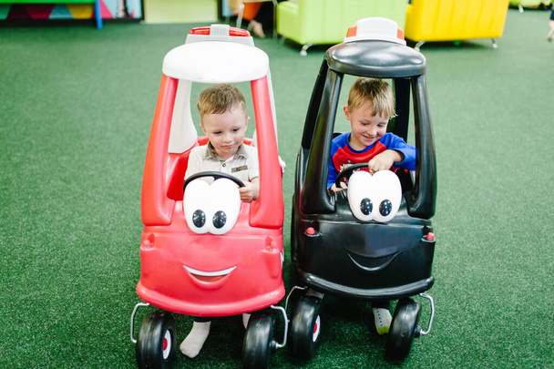 Little kids the boys, child rides on a red, black big car on the road. Close up. The baby is driving the car and played in a children's playroom on a birthday party. - Фото, изображение