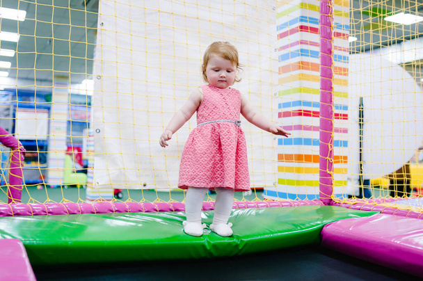 A little baby girl 1-2 years playing and jumping on a trampoline in a children's playroom for her birthday. entertainment centre. - Fotó, kép