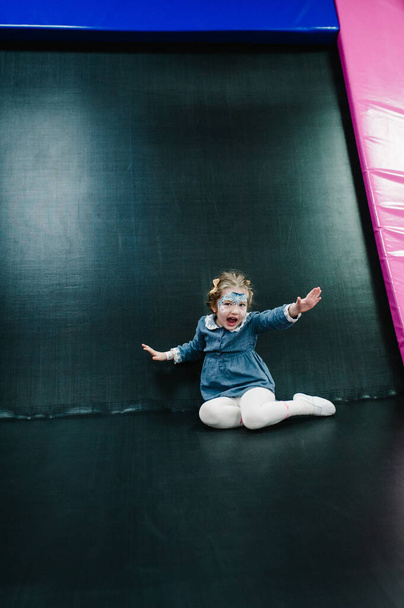 Portrait little cute child girl 3-4 years playing and jumping on trampoline in children's playroom, indoors playground on birthday party. Active girl having fun at sport centre. - Φωτογραφία, εικόνα