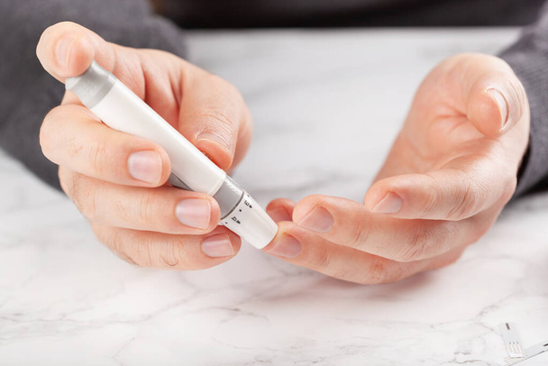 血糖値計で血糖値やケトンのレベルを確認するために、指にランセットを使用して手。糖尿病ケトダイエット｜家庭での健康管理 - 写真・画像