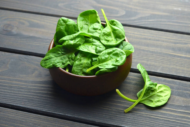 Fresh spinach leaves in wooden bowl over old wooden table. Healthy vegan food. Green living and eco-conscious concept. - 写真・画像