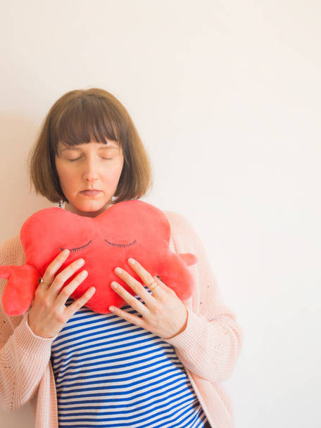 Mladá žena objímající červené srdce ve tvaru plyšové hračky - Fotografie, Obrázek